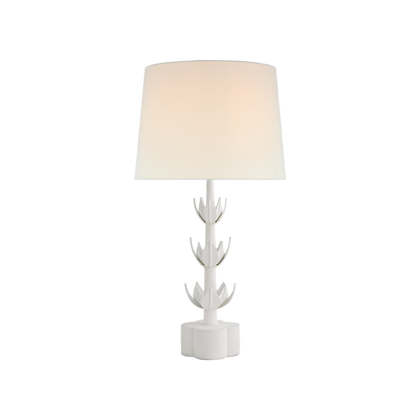 A modern white table lamp with a sculptural, flower-like base and a tapered drum shade, shown illuminated against a plain white background.