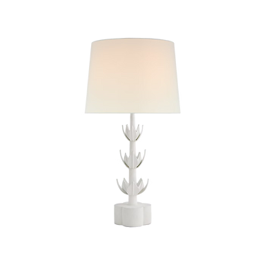 A modern white table lamp with a sculptural, flower-like base and a tapered drum shade, shown illuminated against a plain white background.