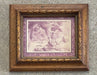 A framed art print featuring a vintage-style illustration of a figure in a landscape in muted purple and beige tones, set within an ornate, distressed brown wooden frame.