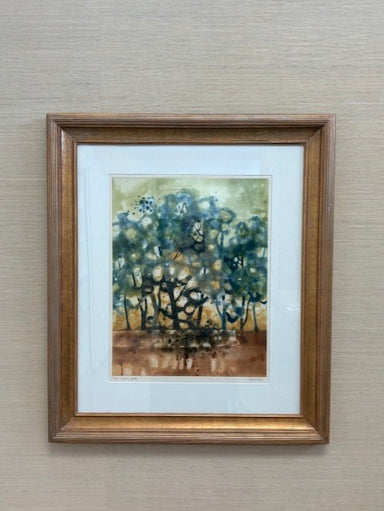 Framed painting of a forest scene with trees in blue and green on a beige wall.