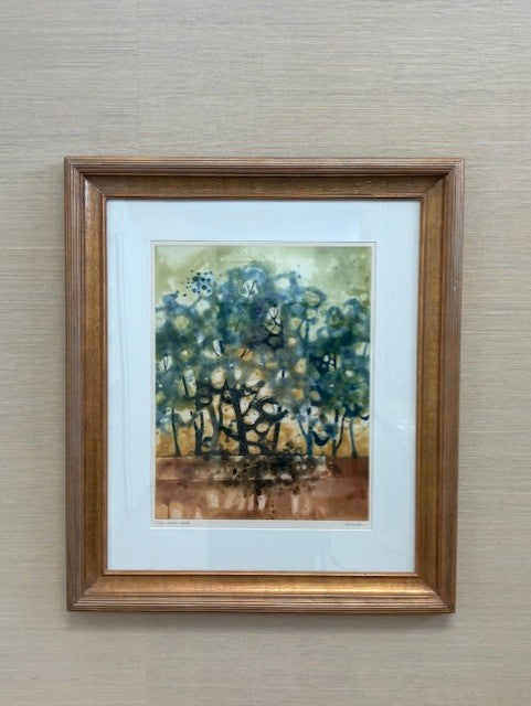 Framed painting of a forest scene with trees in blue and green on a beige wall.