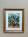 Framed painting of a forest scene with trees in blue and green on a beige wall.