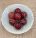 Red cricket balls with white stitching in a stone bowl on a wooden surface