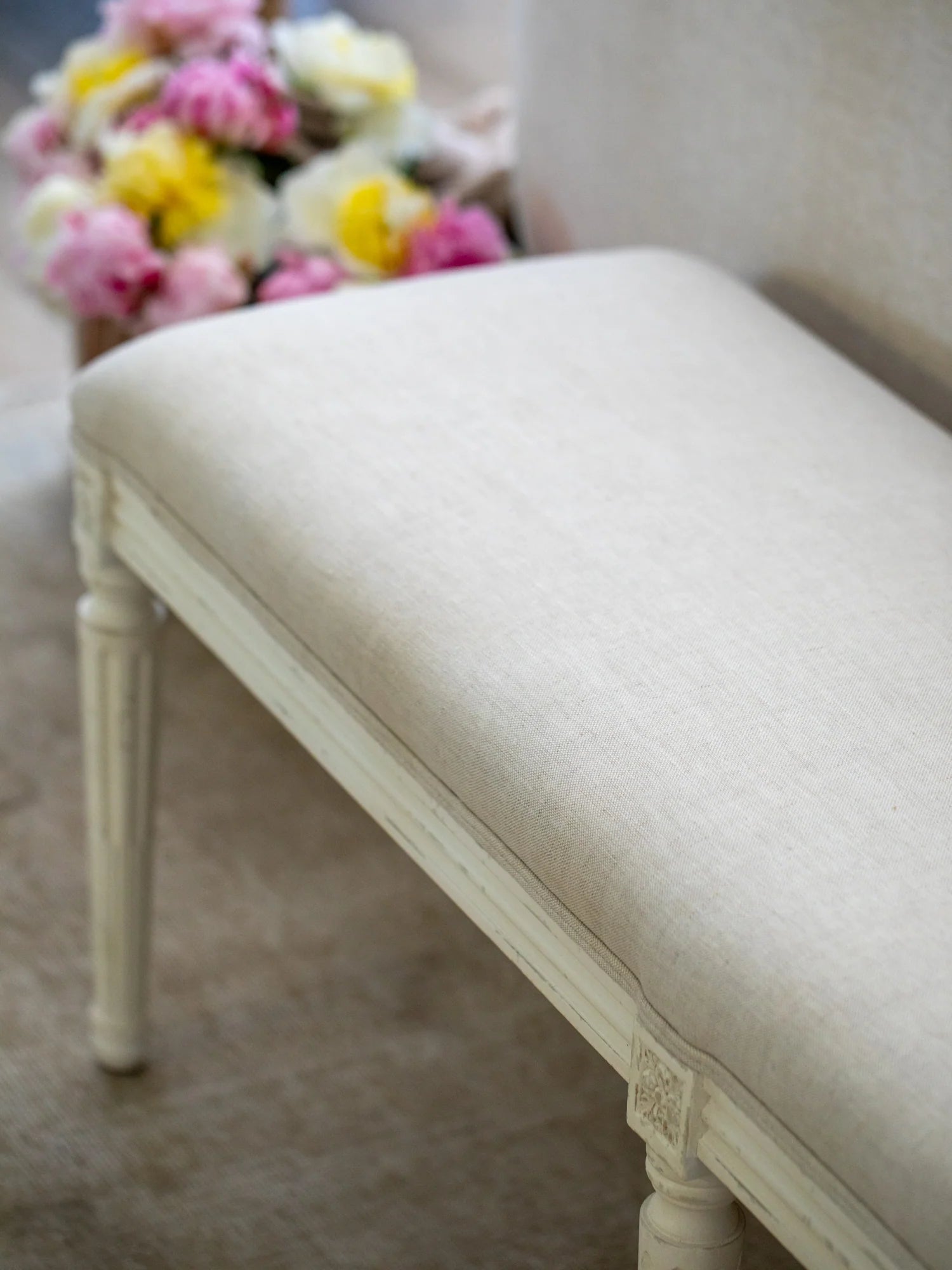 Linen upholstered bench with floral arrangement in the background