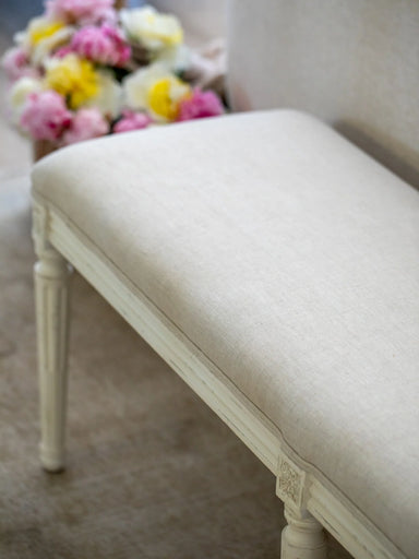Linen upholstered bench with floral arrangement in the background