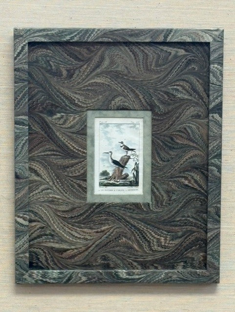 Decorative frame with wavy pattern containing a smaller framed picture of birds on a wooden surface.
