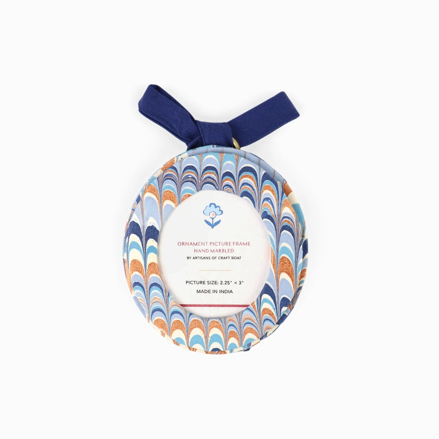 An oval-shaped fabric ornament picture frame with a blue, orange, and white wavy pattern, featuring a navy blue hanging ribbon and a white paper label in the center.