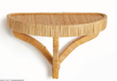 A natural woven rattan wall shelf with a semi-circular oval design and three curved support legs, shown against a plain white background.
