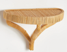 A natural woven rattan wall shelf with a semi-circular oval top and three curved support legs, shown against a plain white background.