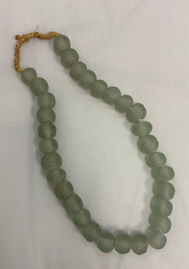 A strand of matte, round, light green-gray beads with a tan cord tie, laid out on a white fabric background.