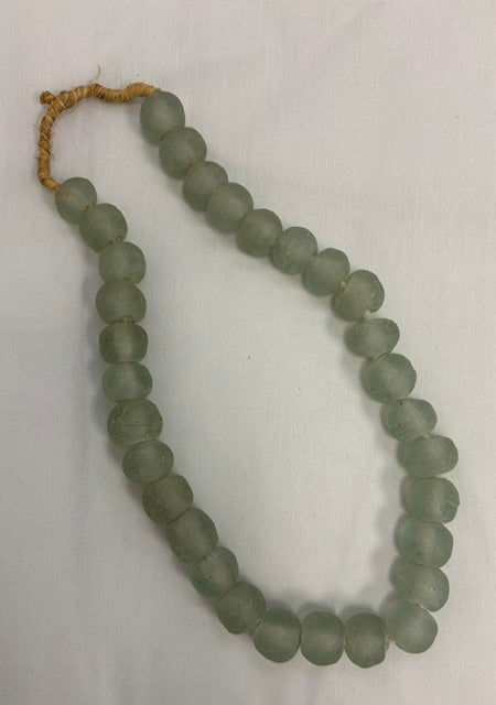 A strand of matte, round, light green-gray beads with a tan cord tie, laid out on a white fabric background.
