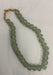 A strand of matte, round, light green-gray beads with a tan cord tie, laid out on a white fabric background.