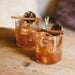 Two cocktails with garnishes on a wooden surface