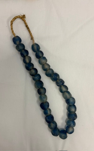 A beaded necklace made of dark blue marbled glass beads with a natural jute loop, displayed on a white fabric background.