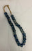 A beaded necklace made of dark blue marbled glass beads with a natural jute loop, displayed on a white fabric background.