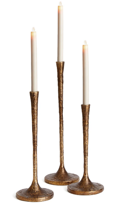 Three textured metallic gold candlestick holders with white taper candles, arranged on a seamless white background.