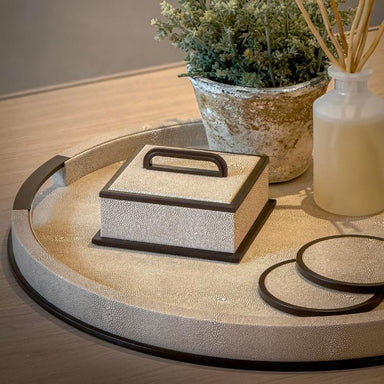 Decorative tray with a textured box, plant, and bottle on a wooden surface