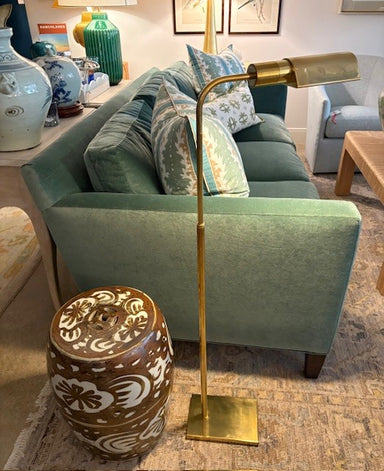 Green sofa with decorative pillows, gold floor lamp, and patterned stool in a living room setting.