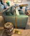 Green sofa with decorative pillows, gold floor lamp, and patterned stool in a living room setting.
