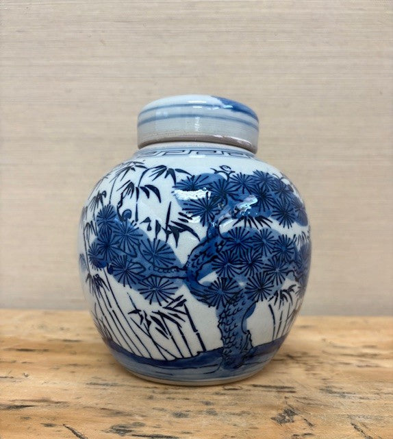 Blue and white ceramic jar with nature-themed design on a wooden surface.