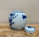 White ceramic jar with blue floral and bird designs on a wooden surface.