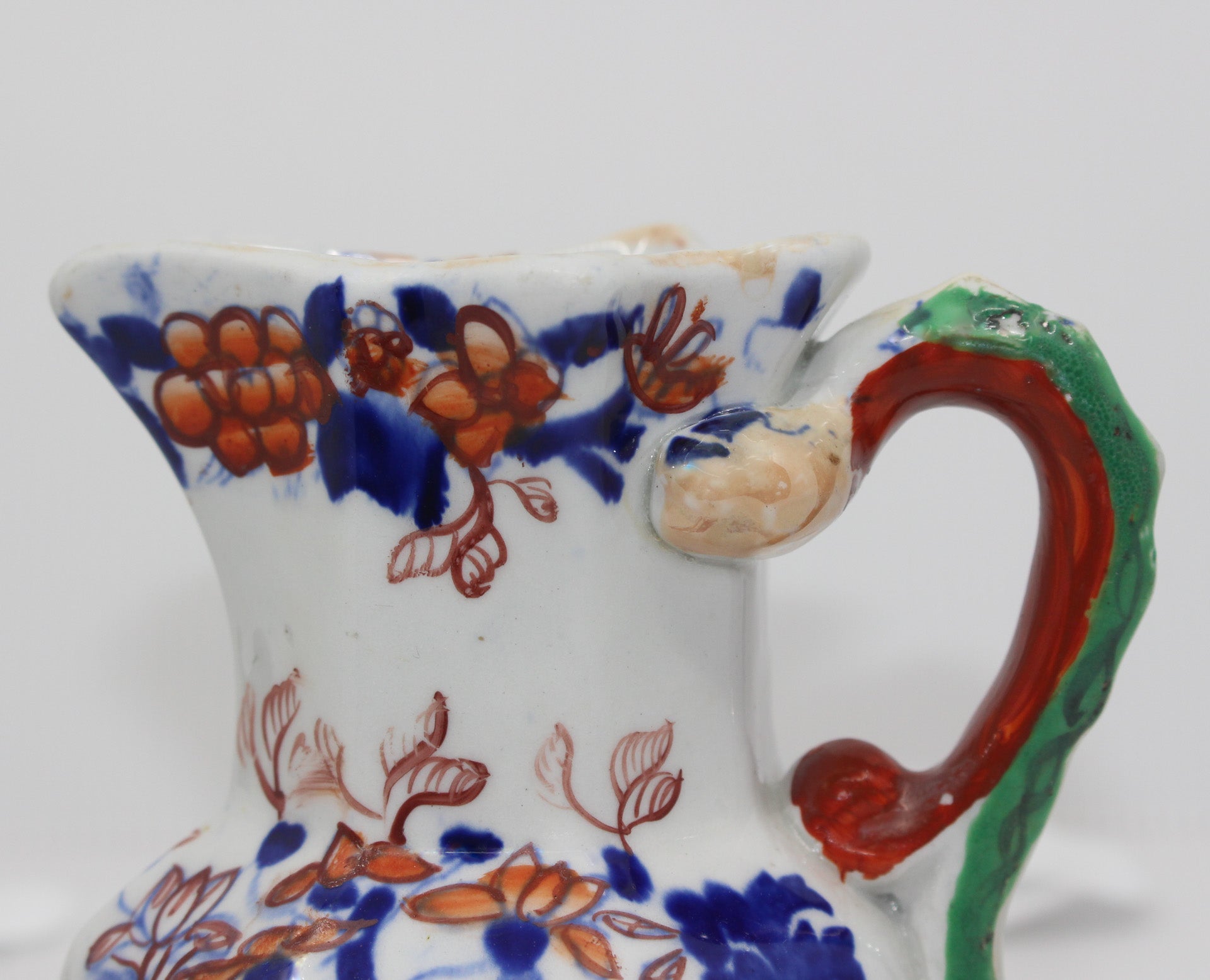 Decorative ceramic pitcher with floral patterns and a red handle on a white background