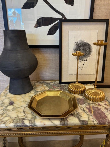 Decorative items including a black vase, gold tray, and candle holders on a marble surface with framed artwork in the background.