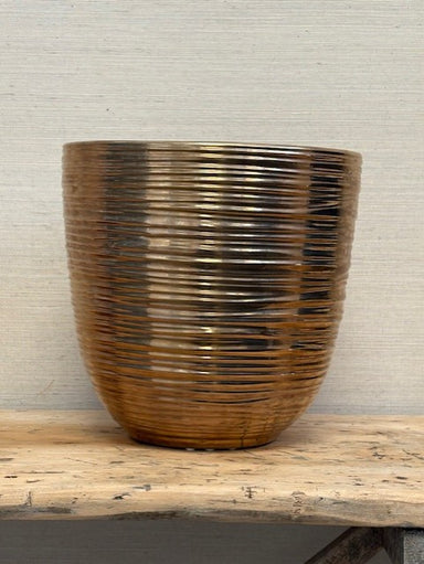 Gold ribbed planter on a wooden surface with a neutral background