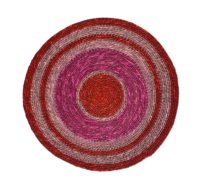 Round woven mat with concentric circular pattern in red and pink on a white background