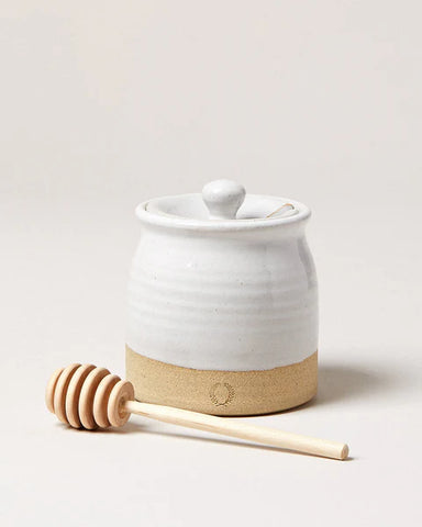 White ceramic honey jar with wooden dipper on a light background