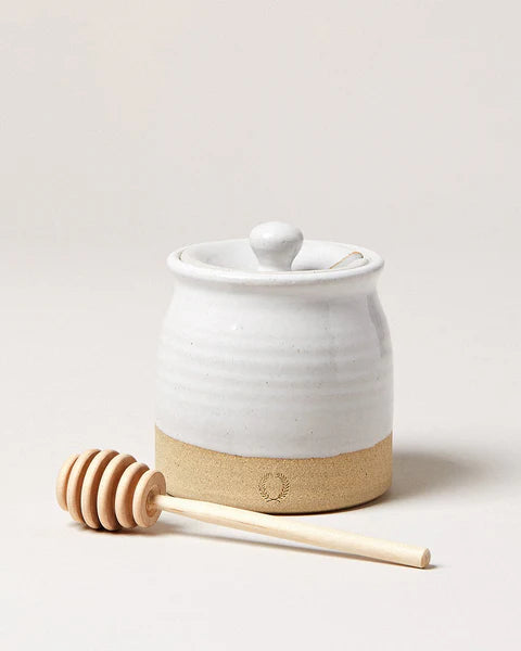 White ceramic honey jar with wooden dipper on a light background