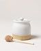 White ceramic honey jar with wooden dipper on a light background