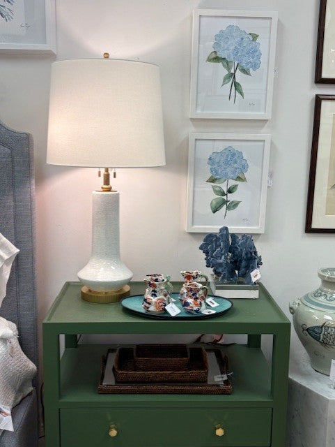 Green nightstand with lamp, decorative items, and framed floral art on a wall.