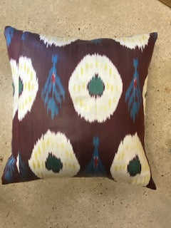 A square-shaped decorative pillow with a geometric ikat pattern in purple, blue, and beige colors.