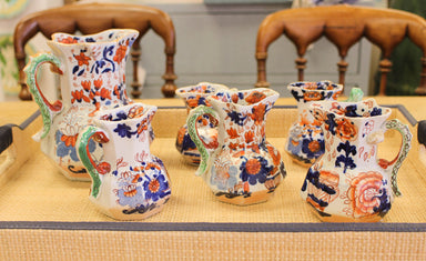 Set of ceramic pitchers with floral patterns on a wooden table.