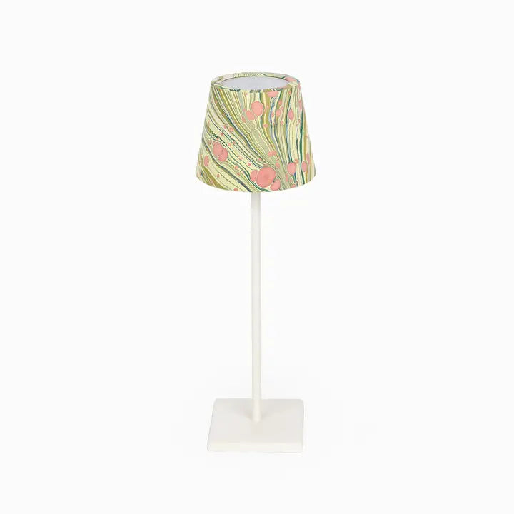 A table lamp with a white metal stand and square base, featuring a tapered fabric shade decorated with a green, yellow, and pink abstract floral pattern.