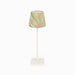 A table lamp with a white metal stand and square base, featuring a tapered fabric shade decorated with a green, yellow, and pink abstract floral pattern.