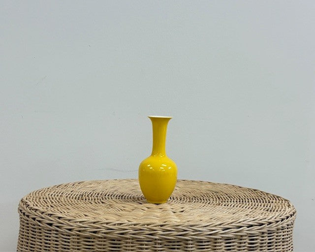 Yellow long neck vase on wicker table with white wall background