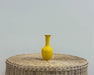 Yellow long neck vase on wicker table with white wall background