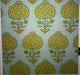 A close-up of a patterned fabric or wallpaper showing a repeating mid-century floral motif in mustard yellow and olive green on a pale sage green background.