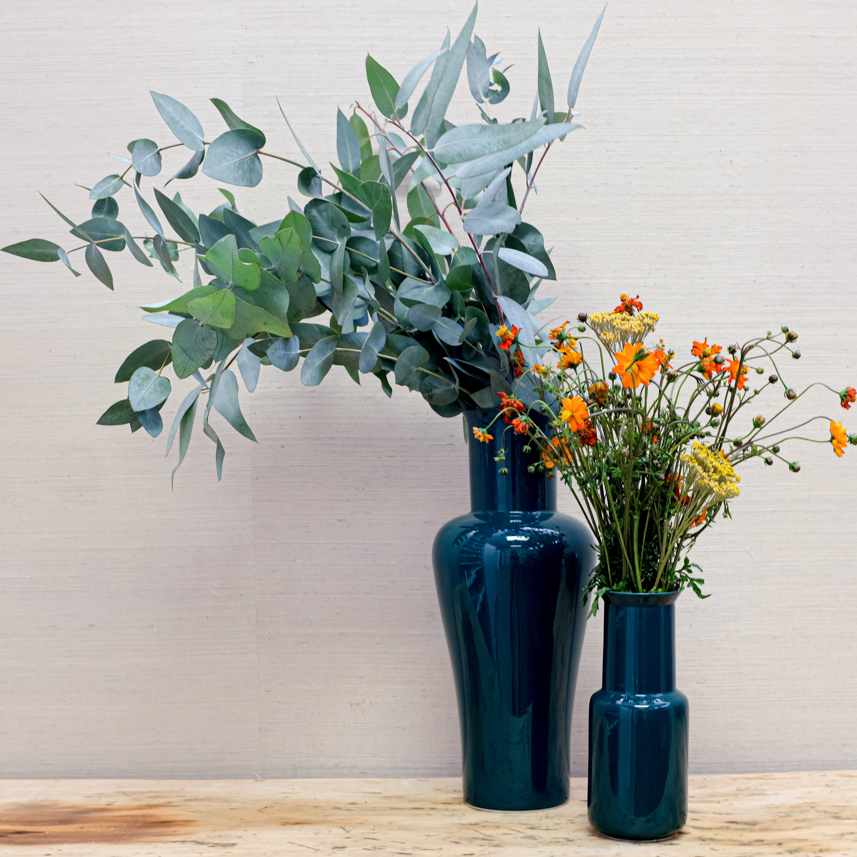 two glossy green vases with eucalyptus and orange flowers