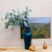 green vase in front of oil painting with pears