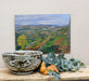 pottery bowl displayed in front of oil landscape painting