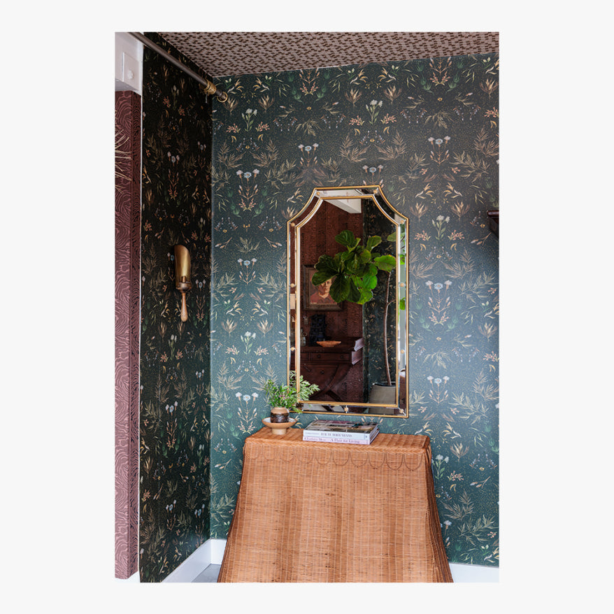 Decorative room with floral wallpaper, a mirror, and a wicker table.