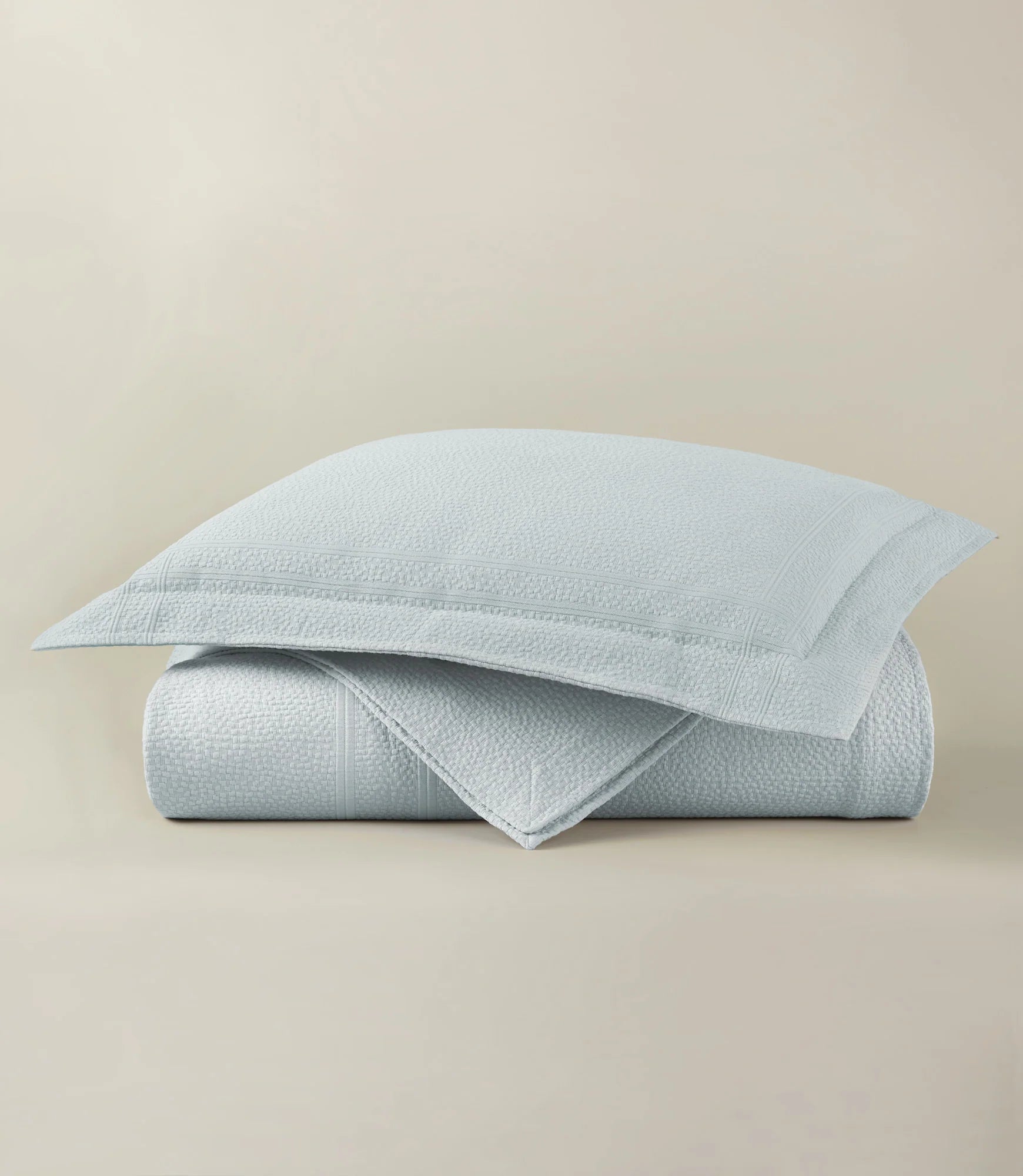 Light blue textured quilt and pillow on a beige background