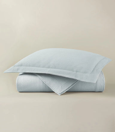 Light blue textured quilt and pillow on a beige background