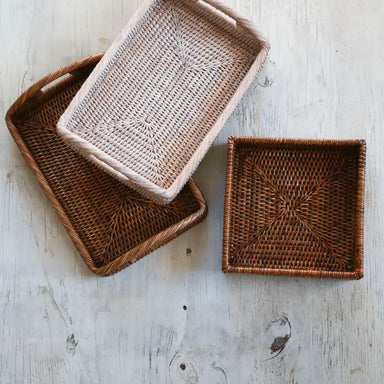 Three woven trays of different sizes on a light wooden surface