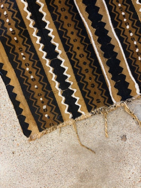 Close-up of a patterned rug with black, gold, and white colors on a concrete floor.