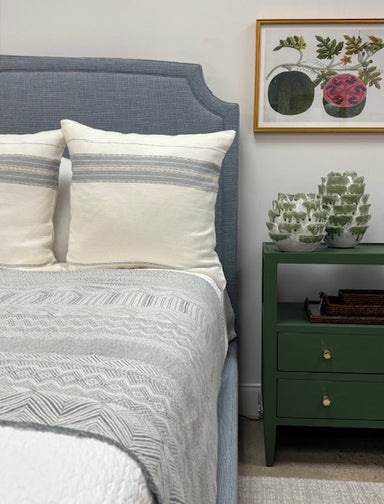 Bedroom with a bed featuring striped pillows and a green nightstand with decorative items.
