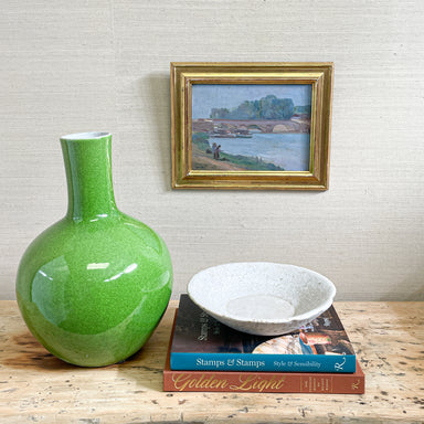 green vase next to book stack with stone bowl and artwork